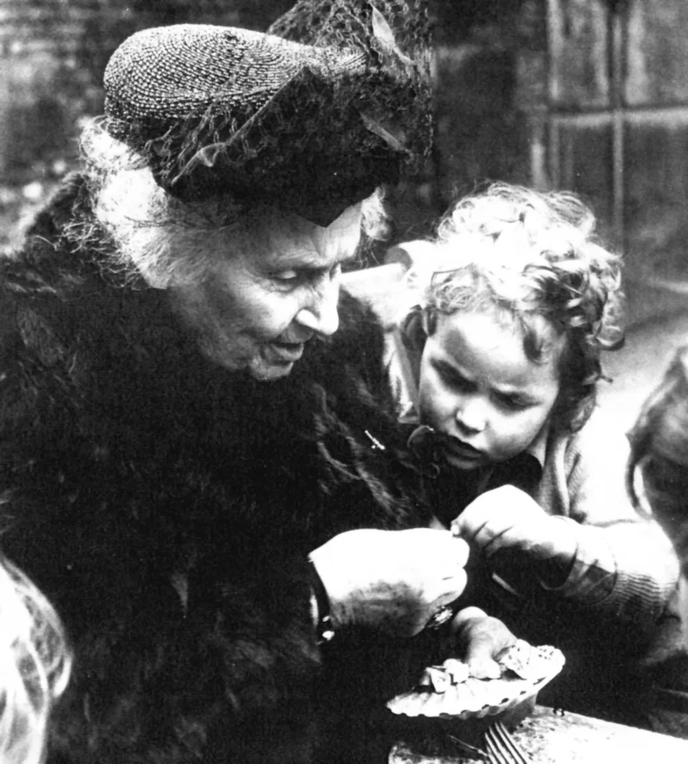 Maria Montessori watching closely as a young child handles small objects.